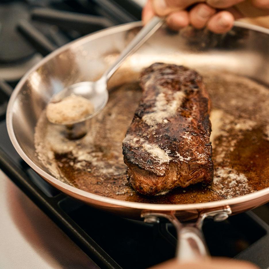 Ein Steak brät in einer Pfanne, während Butter darüber gegossen wird.