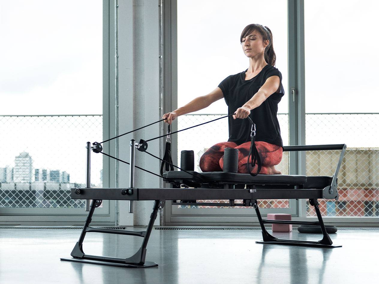 Donna che fa Pilates su una macchina reformer con sfondo cittadino.