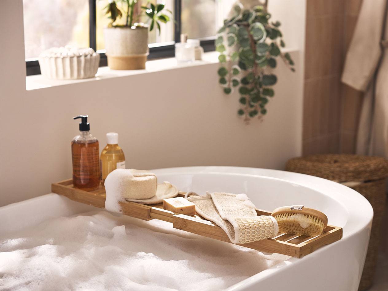 Plateau de bain en bambou avec produits de bain, éponges et brosses au-dessus d'un bain moussant.