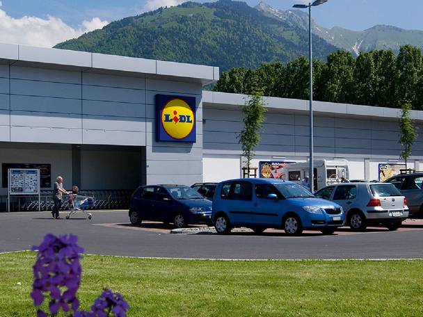 Extérieur d'un supermarché avec parking et montagnes en arrière-plan.