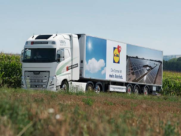 Camion électrique blanc avec remorque affichant des panneaux solaires et le texte 'Le soleil est mon moteur'.