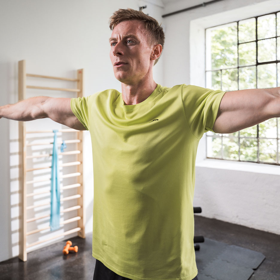 Mann in grünem Sport-T-Shirt trainiert in einem Fitnessstudio.