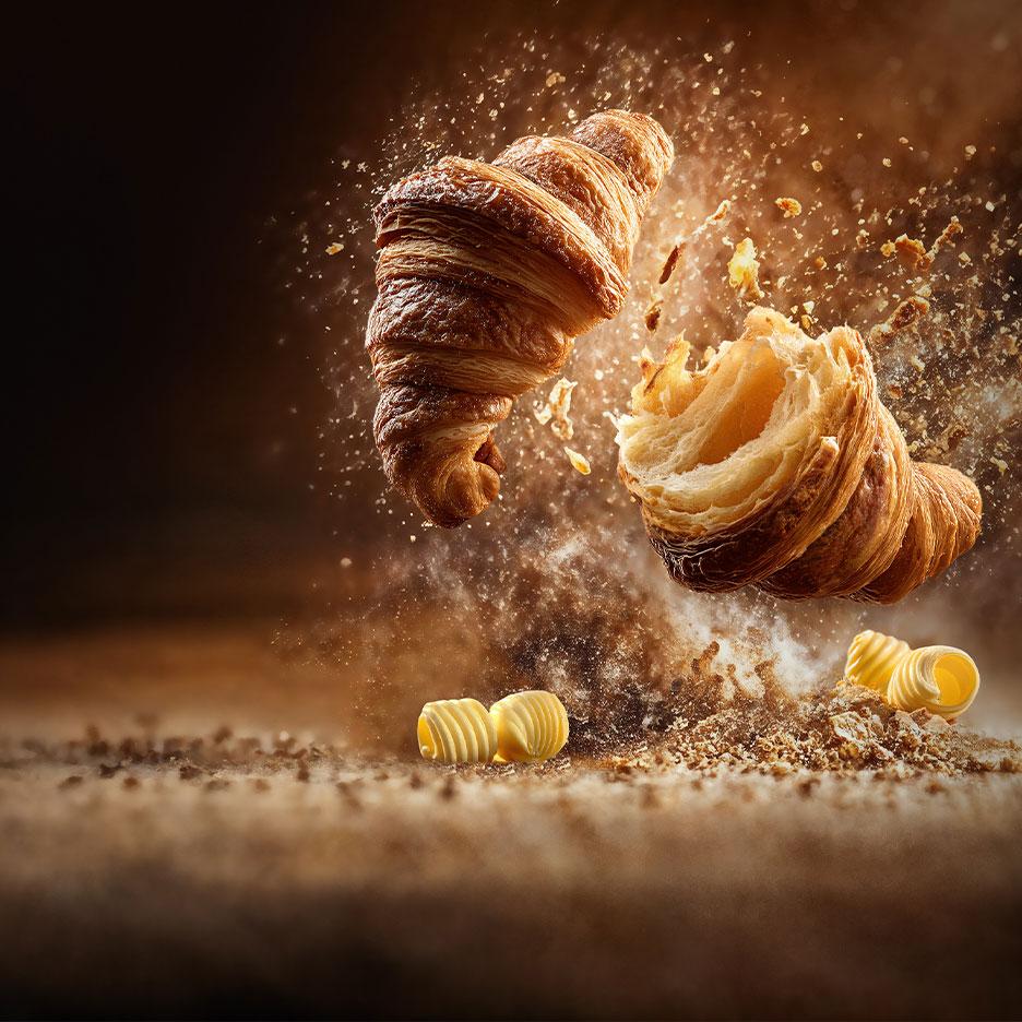 Schwebende Croissants mit Krümeln und Butterröllchen.