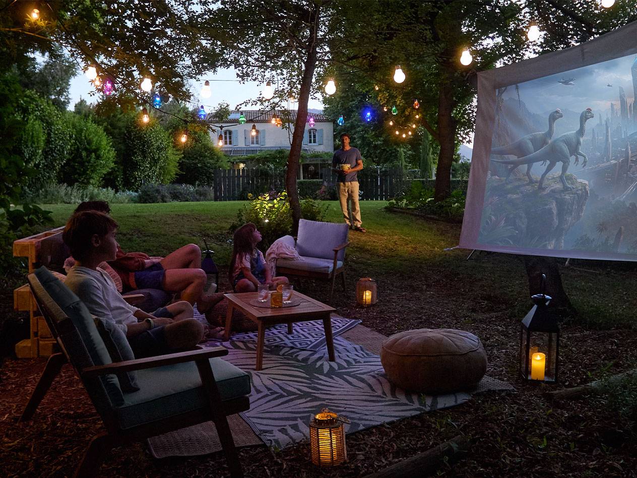 Famiglia che si gode una serata cinema all'aperto con luci a catena e comodi mobili da giardino.