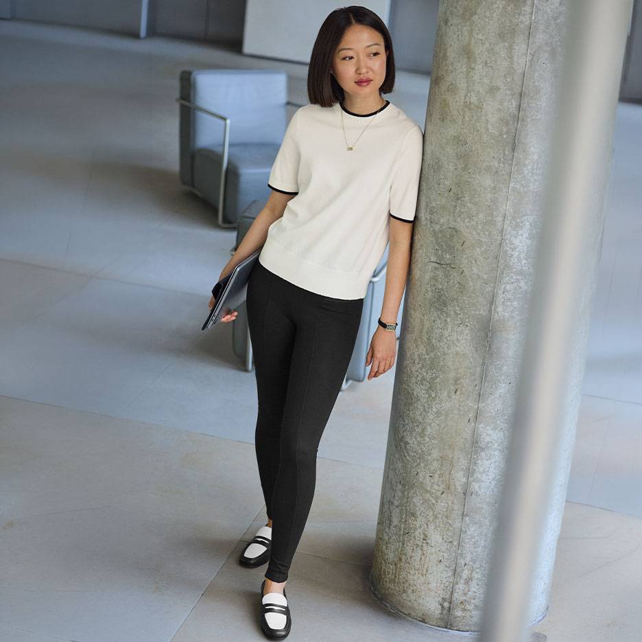 Femme en haut blanc à manches courtes avec liseré noir, leggings noirs et mocassins bicolores.