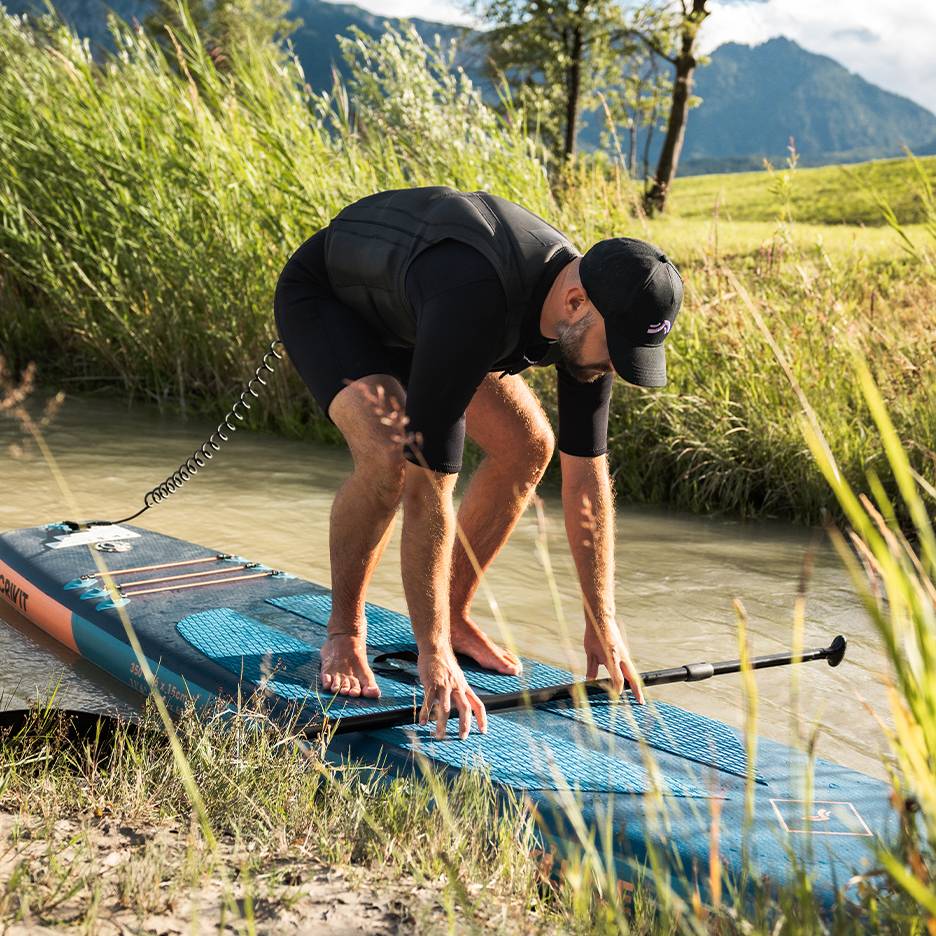 Uomo in muta e giubbotto di salvataggio si prepara per lo stand-up paddle su un fiume.