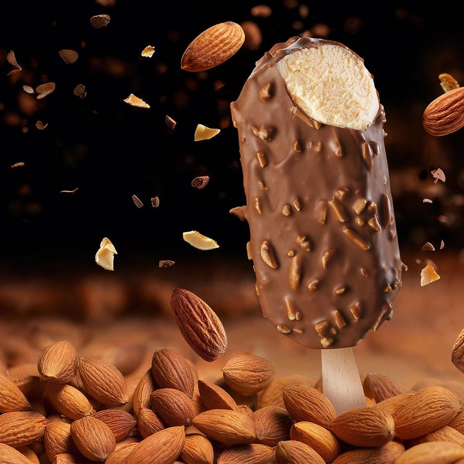 Schokoladen-Eis am Stiel mit Mandeln, einige fallen und andere liegen am Boden.