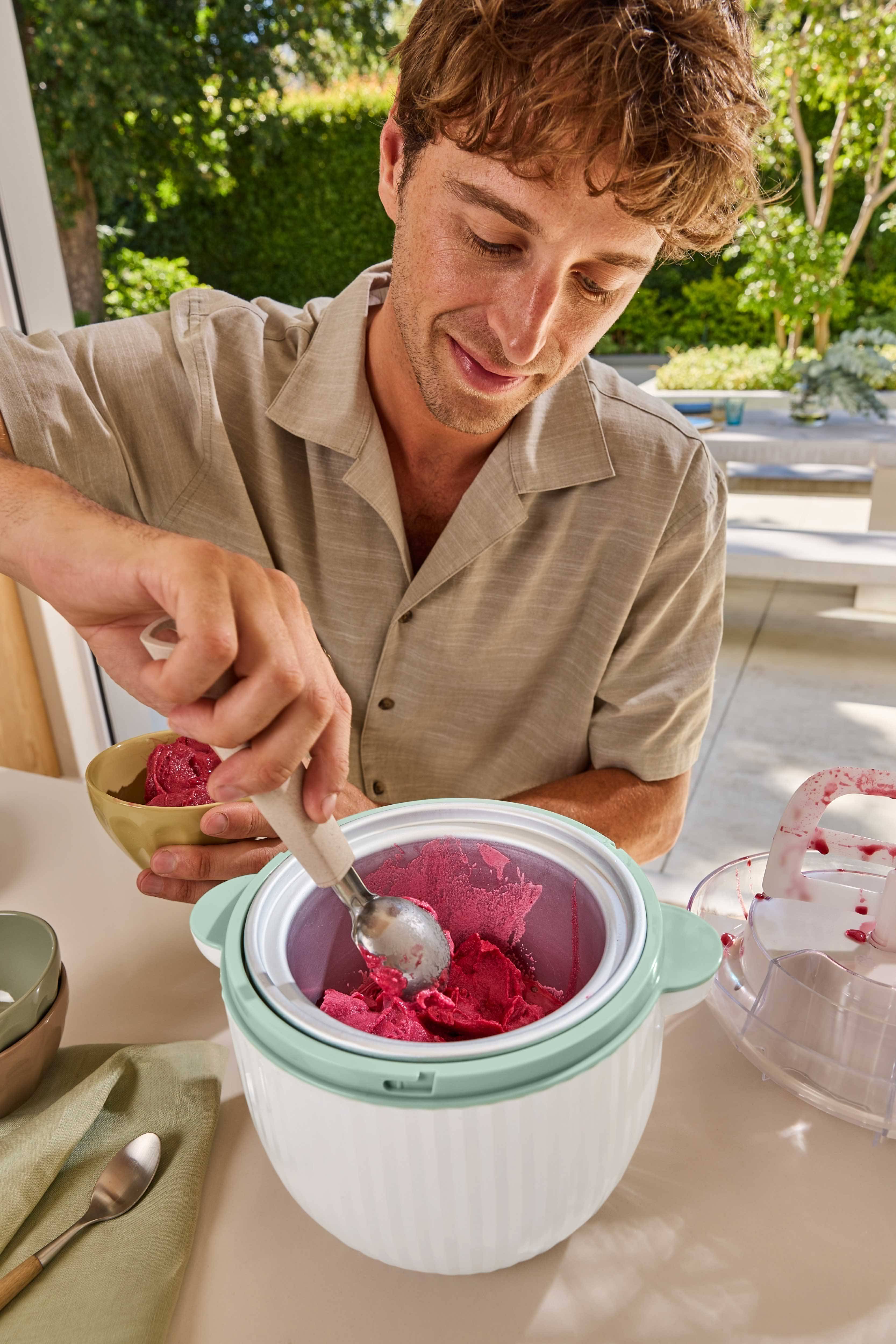 Mann schöpft rotes Sorbet aus einer Eismaschine in eine Schüssel.