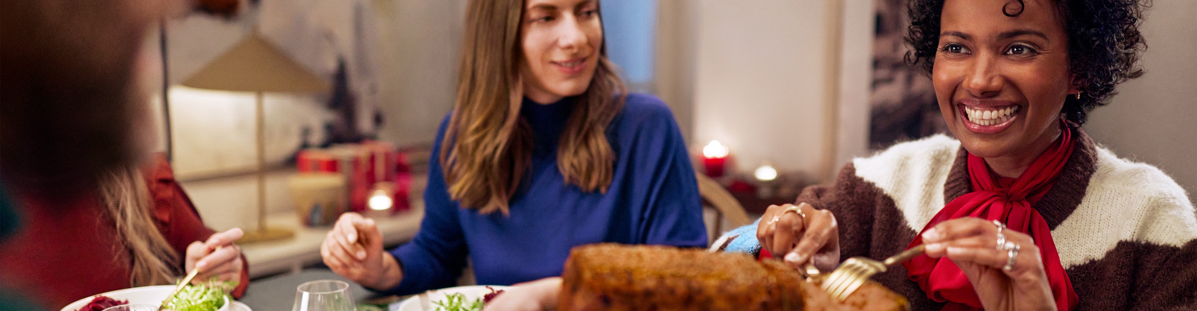 Lachende Freunde am Tisch, die ein festliches Essen mit einem Braten genießen.
