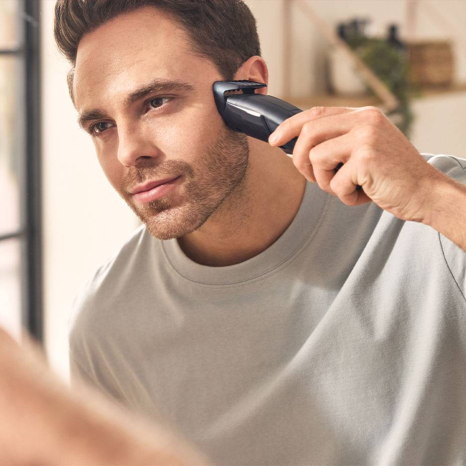 Homme taillant sa barbe avec une tondeuse devant un miroir.
