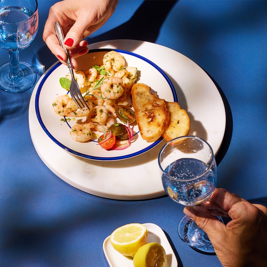 Garnelen mit Kräutern, Tomaten, roten Zwiebeln und geröstetem Brot, serviert mit Zitrone und Getränken.