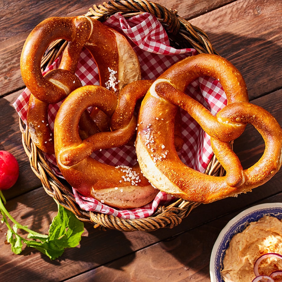 Bretzels salés dans un panier avec une serviette à carreaux, des radis et un bol de tartinade.