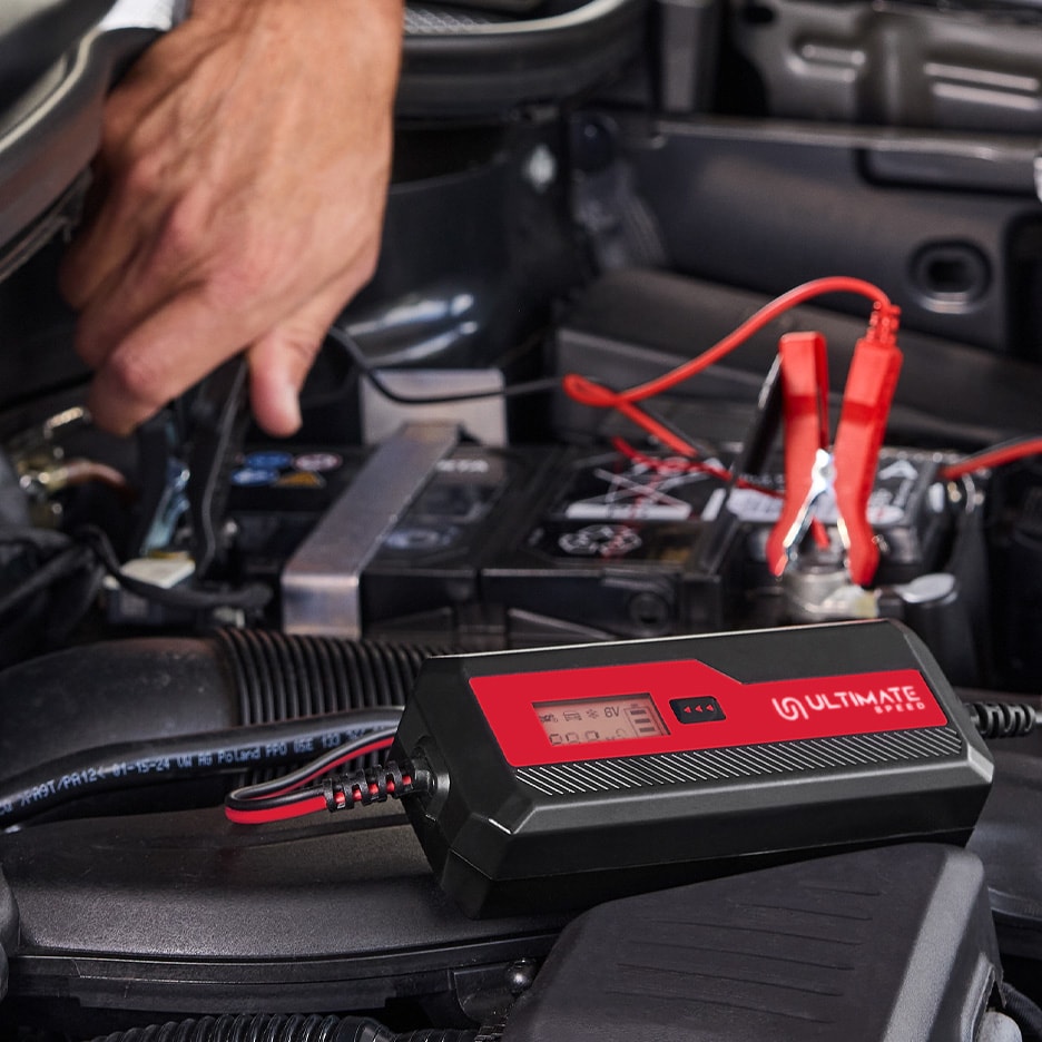Ein schwarzes und rotes Autobatterieladegerät ist an eine Autobatterie angeschlossen.