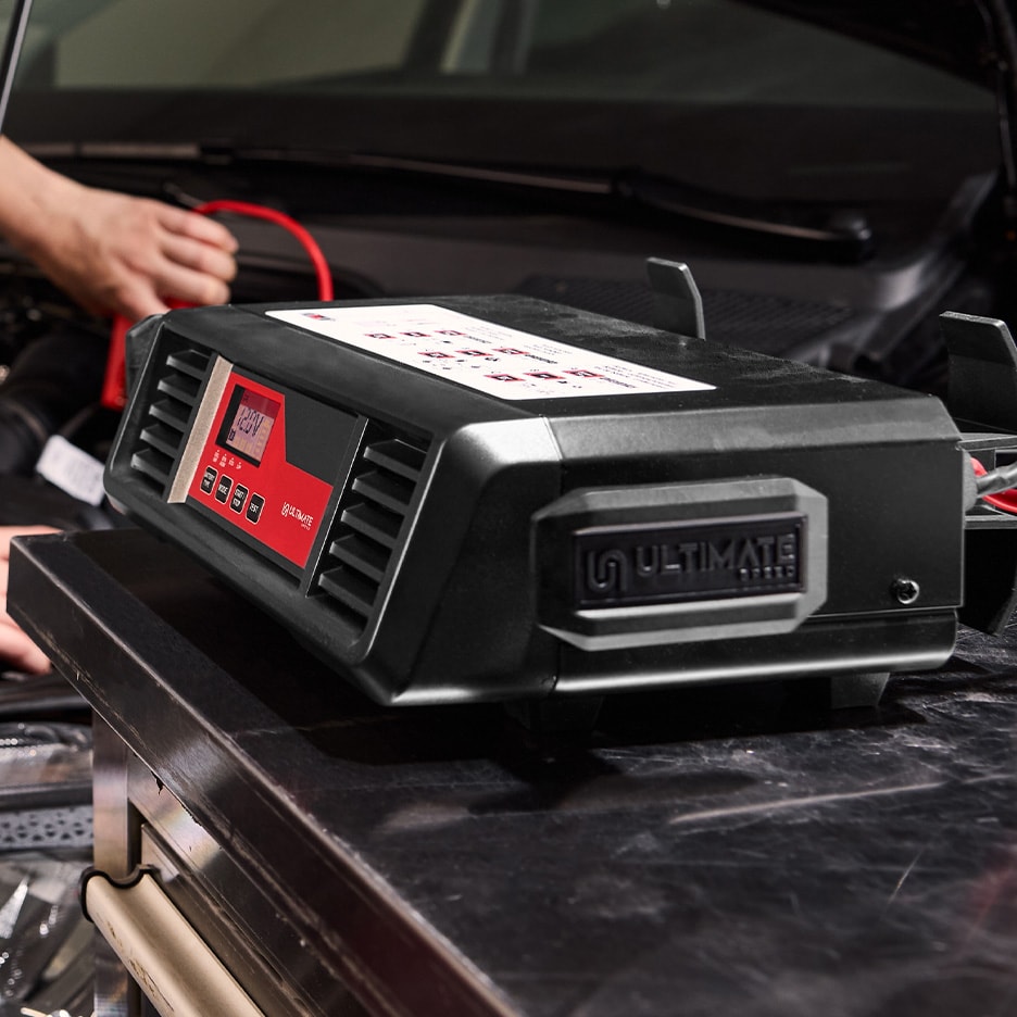 ULTIMATE SPEED Autobatterieladegerät mit Digitalanzeige, an eine Autobatterie angeschlossen.