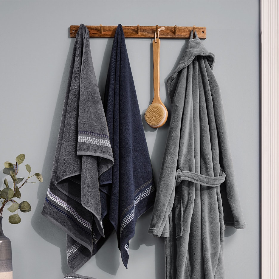 Grauer Bademantel, blaue und graue Handtücher und Badebürste hängen an der Wand.