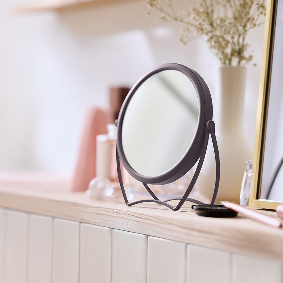 Un miroir de maquillage rond sur une table en bois avec du maquillage et un vase.