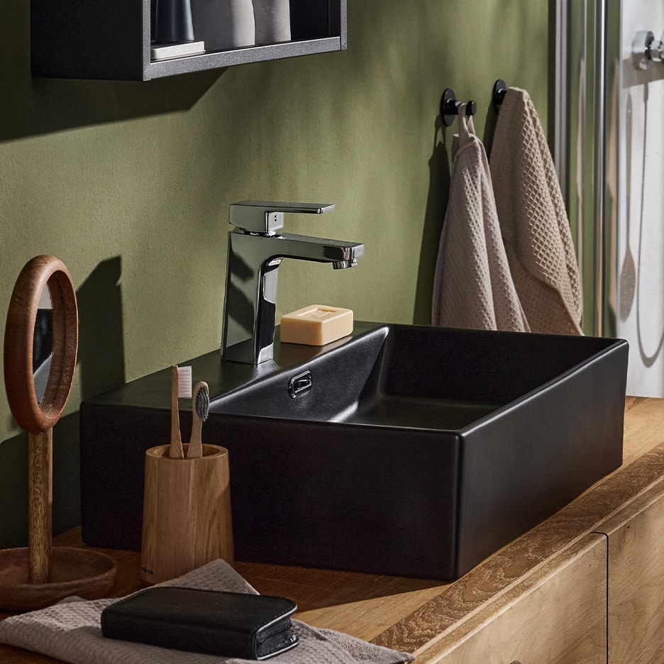 Schwarzes Waschbecken mit Chromarmatur, Seife und Zahnbürsten auf Holzunterschrank.