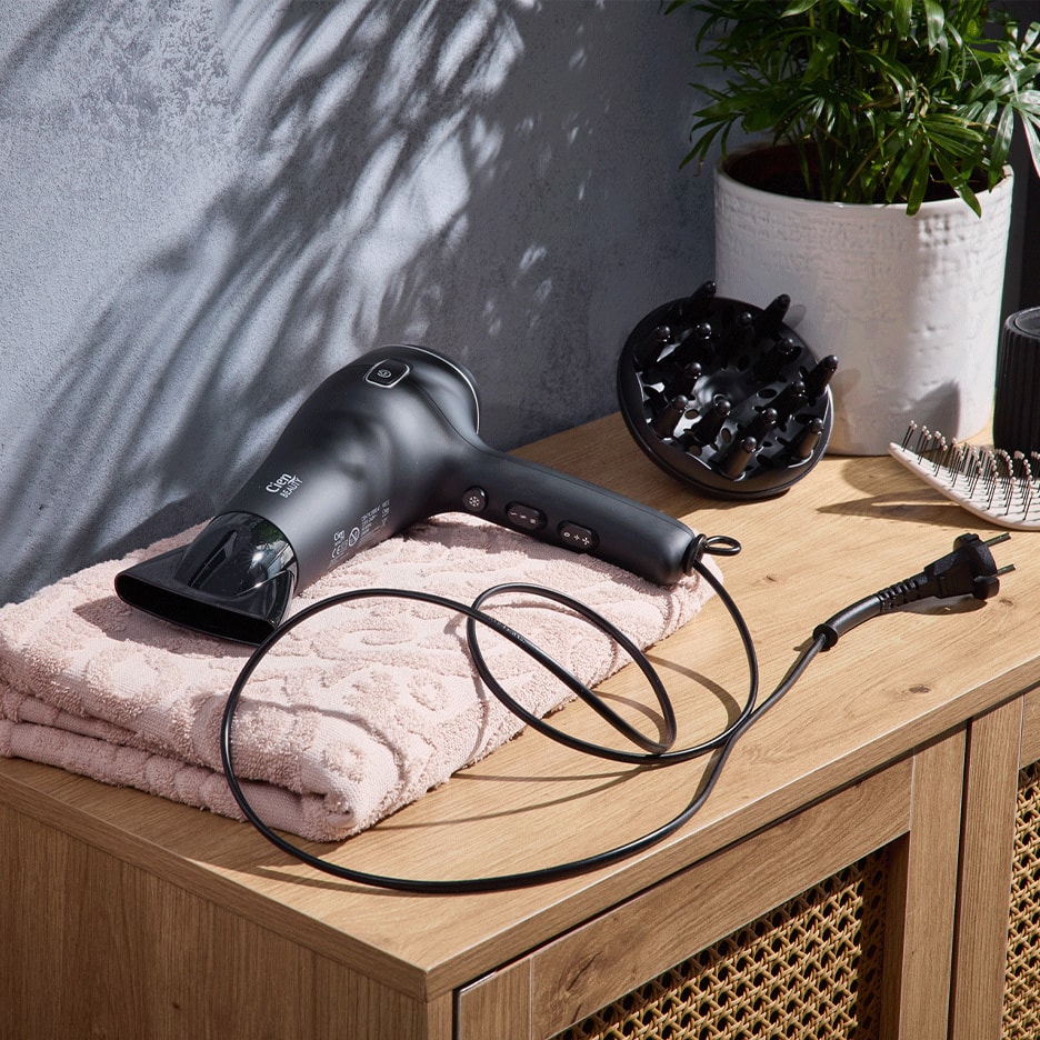 Mattschwarzer Haartrockner mit Diffusor und rosa Handtuch auf einer Holzkommode.