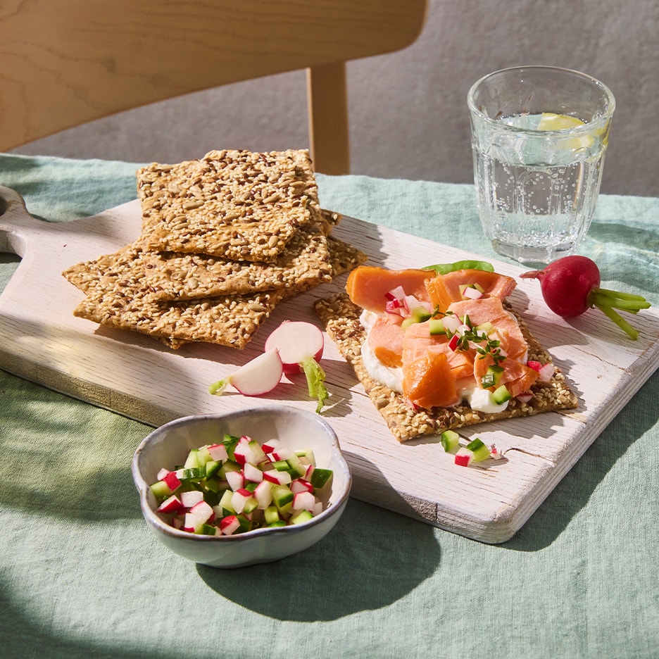 Knäckebrot mit Räucherlachs, Frischkäse und Radieschen auf einem Holzbrett.