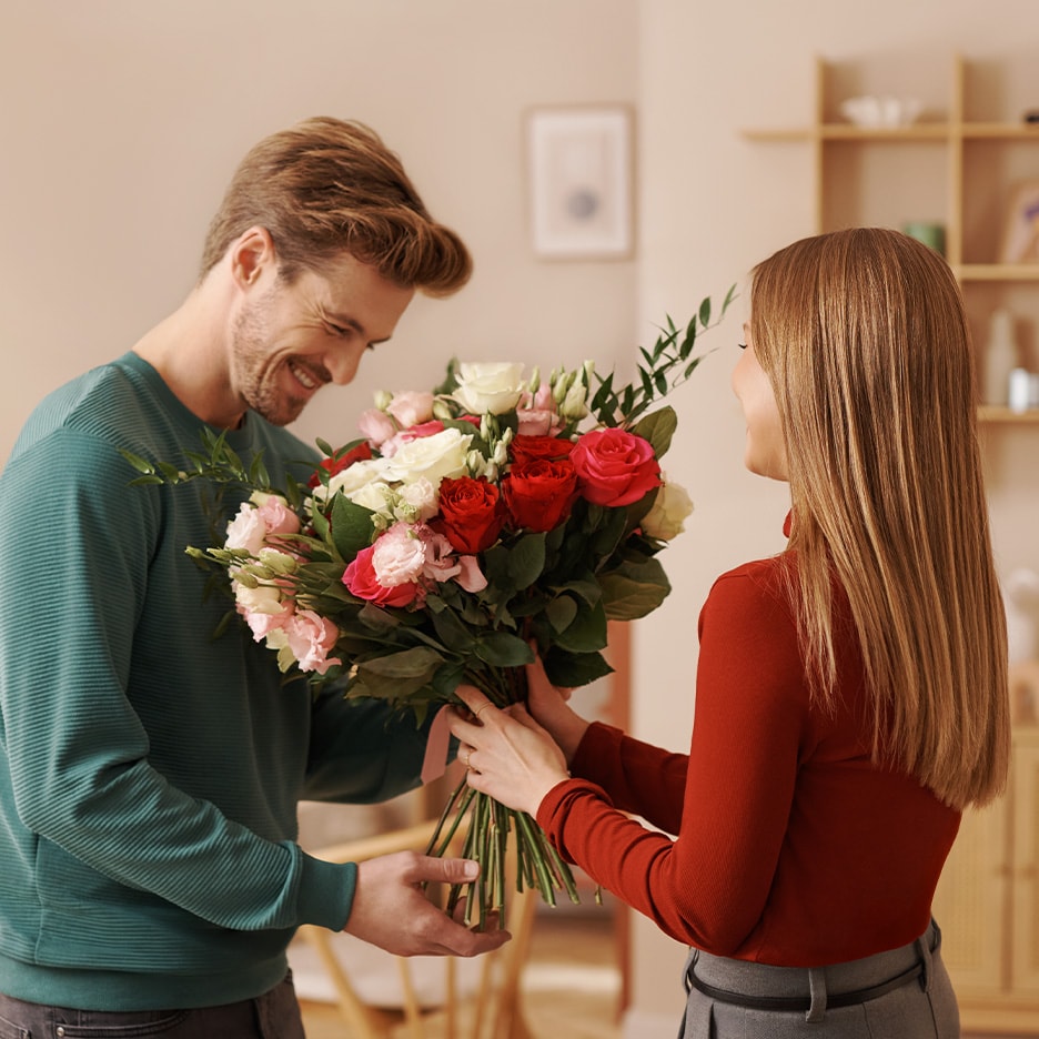 Homme souriant offrant un grand bouquet de roses rouges et roses à une femme.