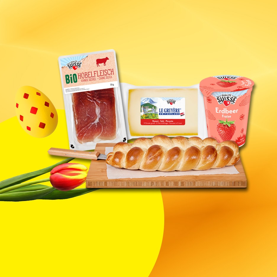 Zopf, Käse, Trockenfleisch und Erdbeerjoghurt auf gelb-orangem Hintergrund mit einem Osterei und einer Tulpe.