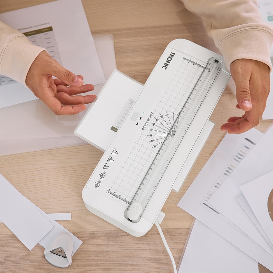 Person laminiert Dokumente mit einem TRONIC Laminiergerät auf einem Holztisch.