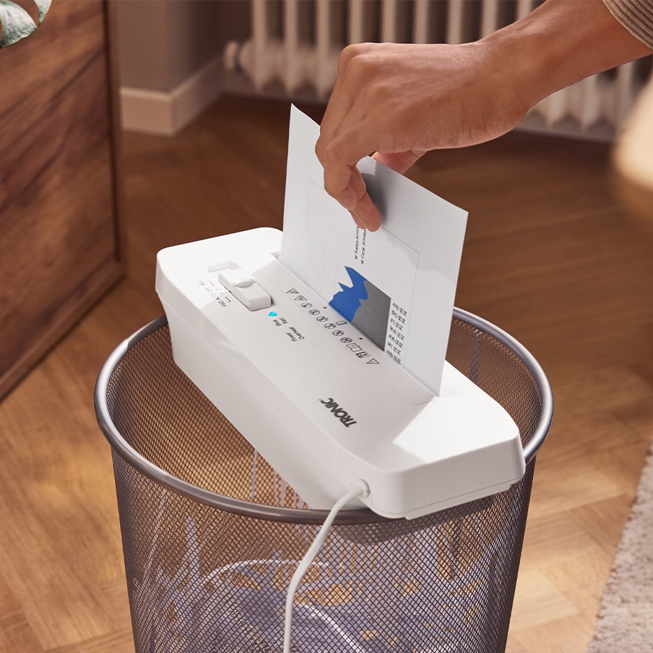 Weißer TRONIC Aktenvernichter auf einem Metallmülleimer, eine Hand führt Papier ein.