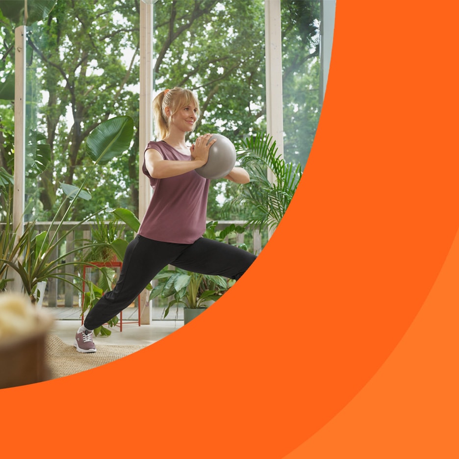 Frau macht Ausfallschritte mit einem Pilatesball in einem hellen Raum mit Pflanzen.