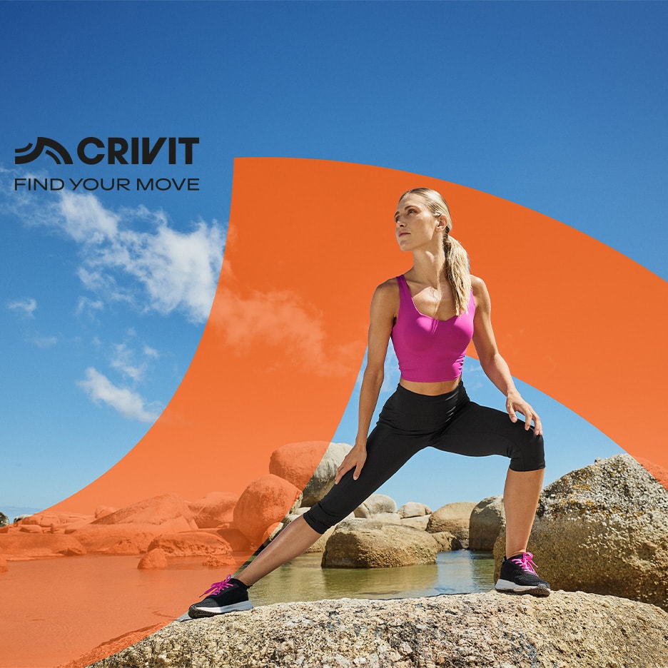 Frau in pinker und schwarzer Sportkleidung dehnt sich auf Felsen, mit blauem Himmel und Wasser.