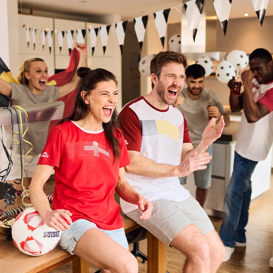 Freunde in Sportbekleidung jubeln beim Fußballschauen, mit einem Ball und Partydekoration.