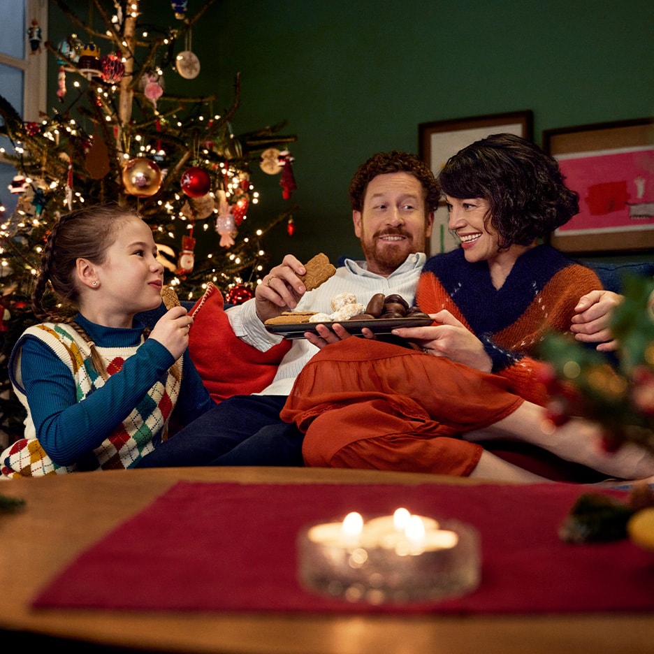 Glückliche Familie teilt Weihnachtsplätzchen und Süßigkeiten am Weihnachtsbaum.