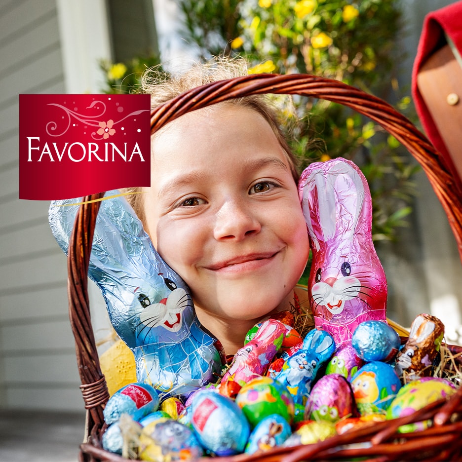 Lächelndes Kind mit Osterkorb voller Schokohasen und Ostereiern.