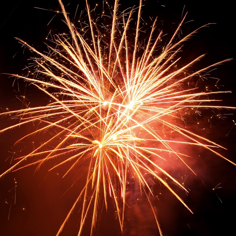 Helle orange und gelbe Feuerwerke explodieren vor einem dunklen Nachthimmel.