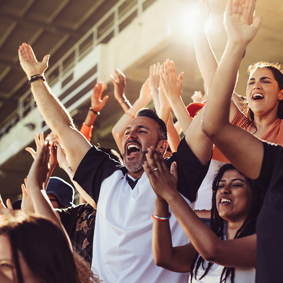 Begeisterte Fans in einem Stadion, die klatschen und jubeln, mit erhobenen Armen.