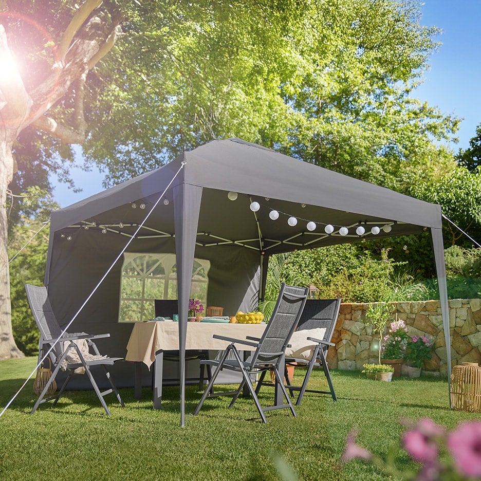 Grauer Gartenpavillon mit Tisch und Klappstühlen, dekoriert mit Lichterketten.