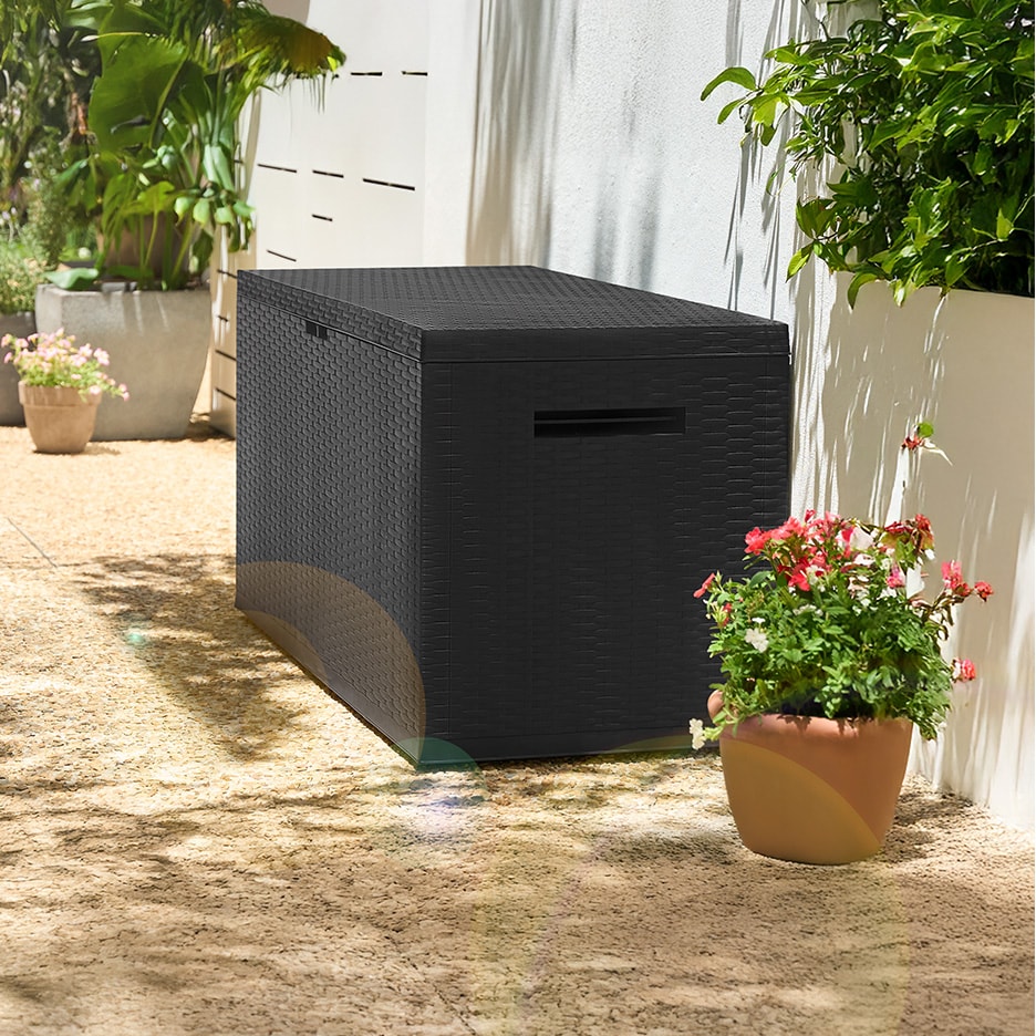 Schwarze Outdoor-Aufbewahrungsbox mit geflochtener Textur auf einer Terrasse mit Topfpflanzen.