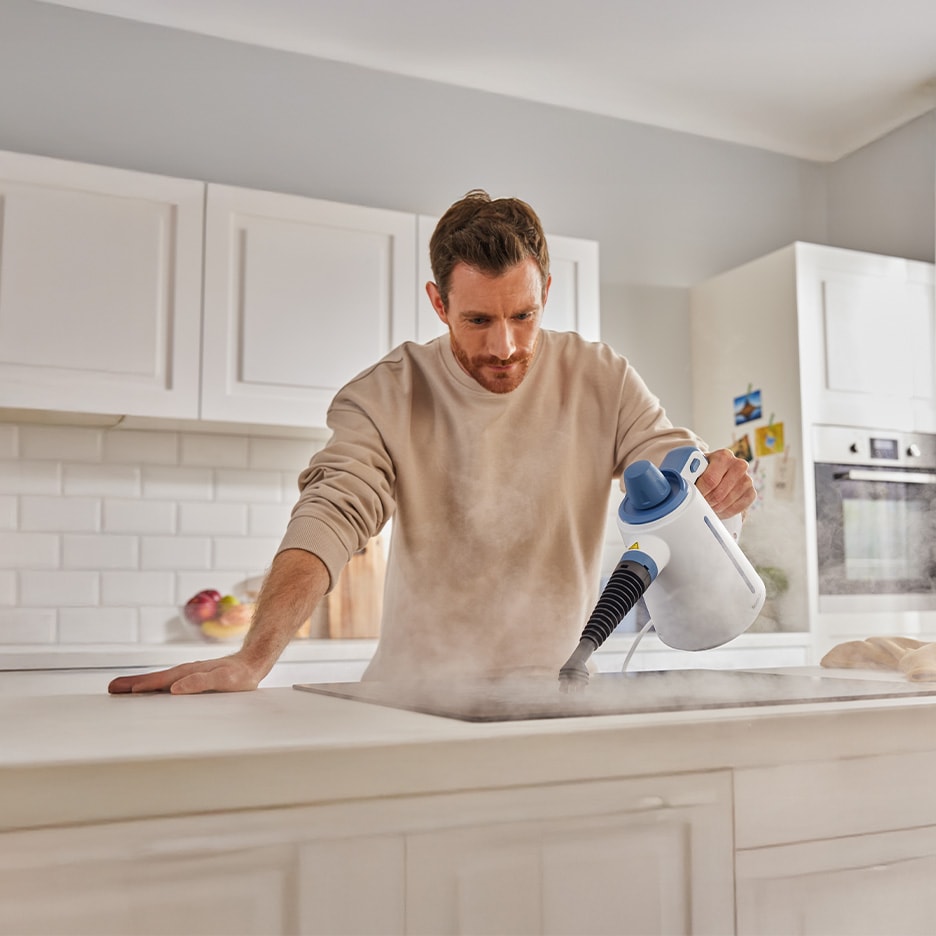 Mann reinigt Kochfeld mit Dampfreiniger in der Küche.