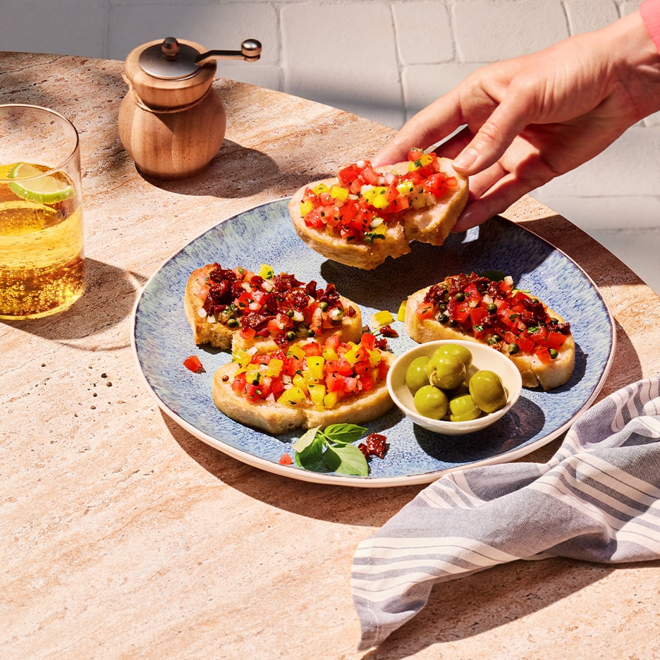 Bunte Bruschetta mit Tomaten, Paprika und Oliven auf einem Steintisch.