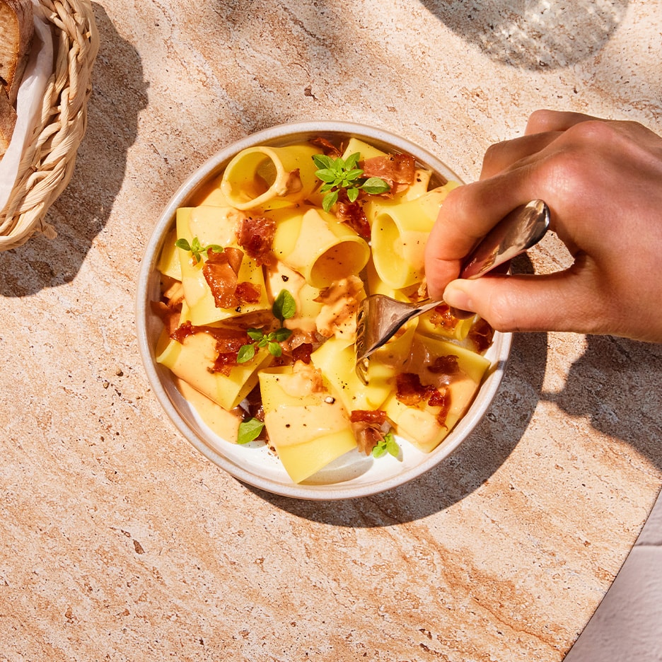 Calamarata-Nudeln Carbonara mit knusprigem Speck und frischem Basilikum.