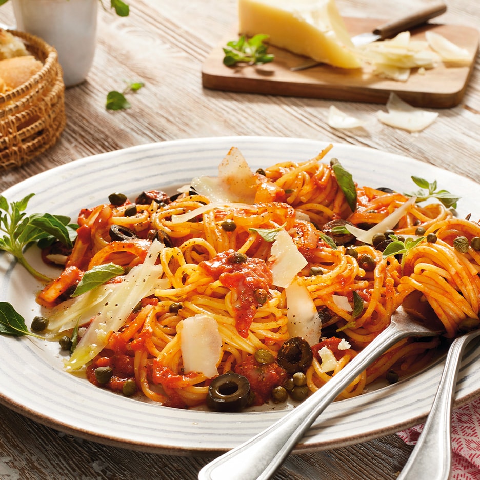 Spaghetti mit Tomatensauce, Oliven, Kapern und Parmesan auf einem Holztisch.
