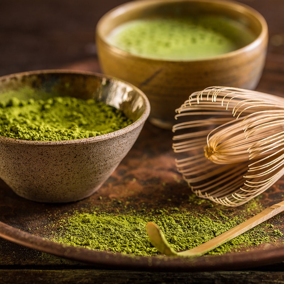 Matcha-Tee-Set mit Pulver, zubereitetem Tee, Bambusbesen und Löffel auf einem Tablett.