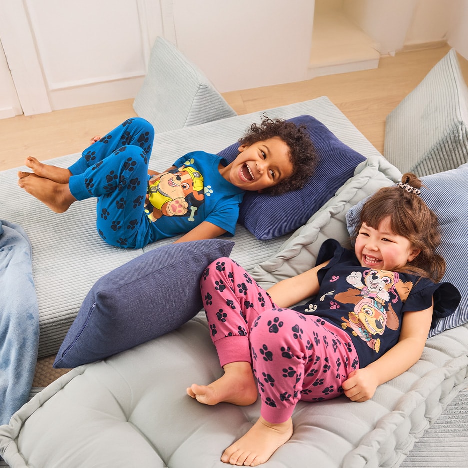 Deux enfants rieurs en pyjama à motifs de pattes, allongés sur des matelas de sol.