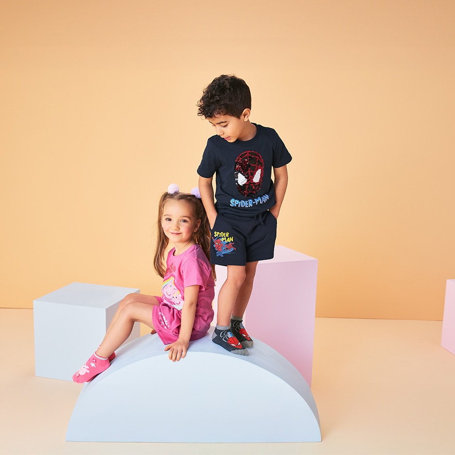 Zwei lächelnde Kinder, ein Junge im Spiderman-Set, ein Mädchen im rosa Kleid.