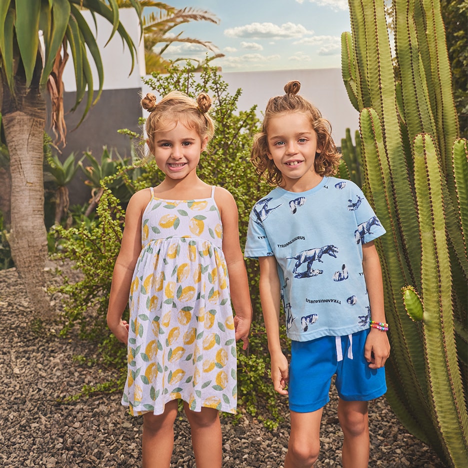 Mädchen in Zitronenkleid und Junge in Dinosaurier-T-Shirt, blauen Shorts.