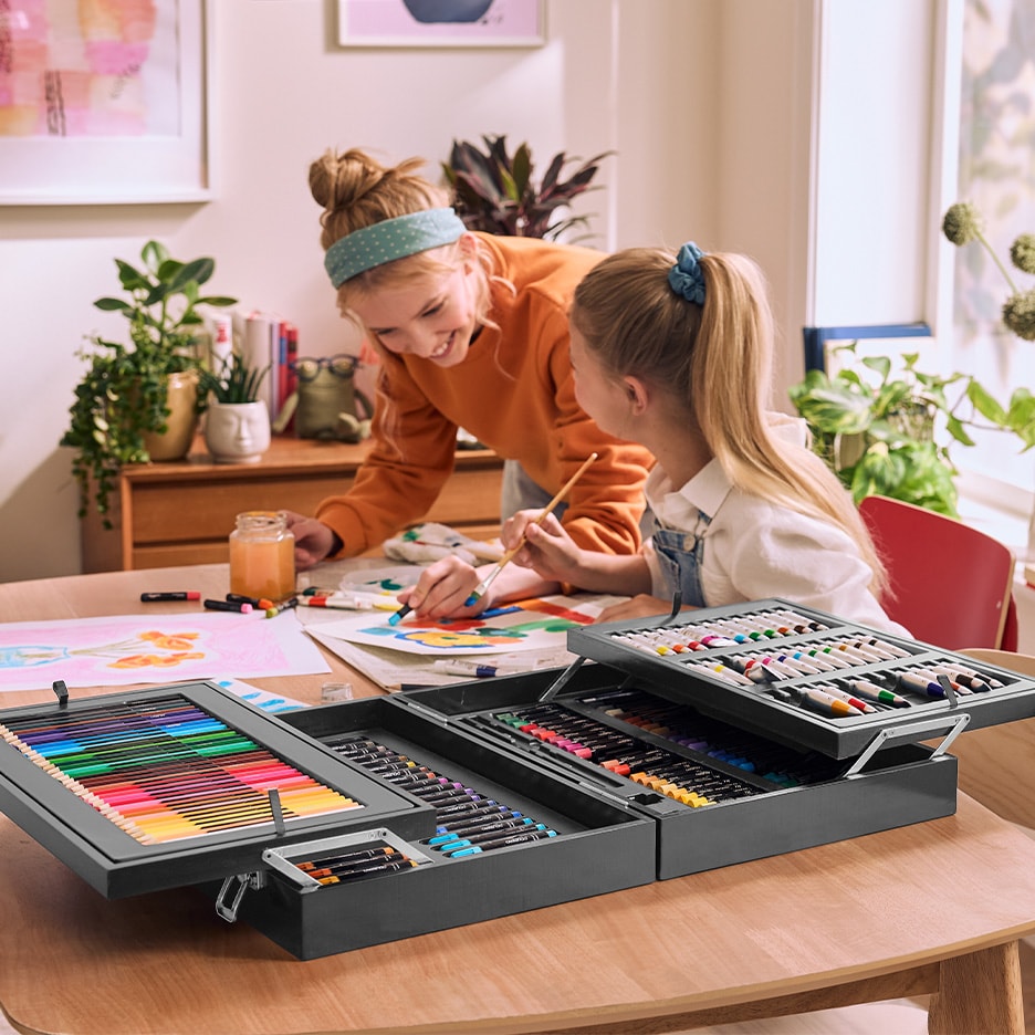 Zwei Kinder malen mit einem großen Kunstset an einem Holztisch.