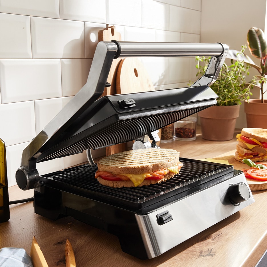 Ein offener Panini-Grill mit einem gegrillten Käse-Tomaten-Sandwich auf einer Küchenarbeitsplatte.