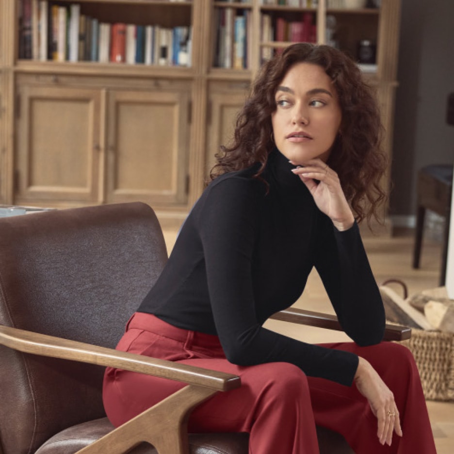 Frau in schwarzem Rollkragenpullover und roter Hose sitzt in einem Ledersessel.