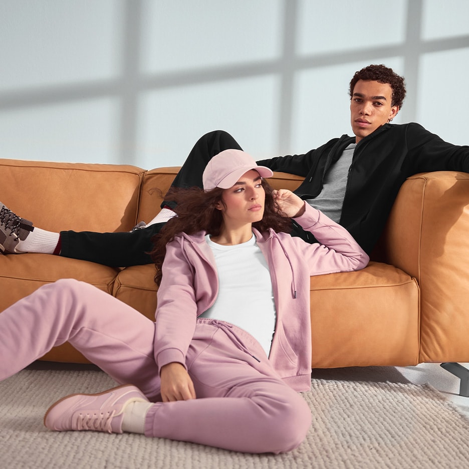 Zwei Personen in Sportanzügen, einer rosa und einer schwarz, entspannen auf einem Sofa und dem Boden.