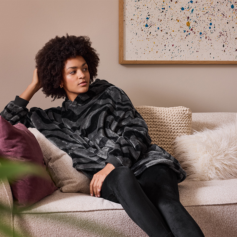 Frau in einem übergroßen Fleece-Kapuzenpullover mit Zebramuster, auf einem Sofa sitzend.