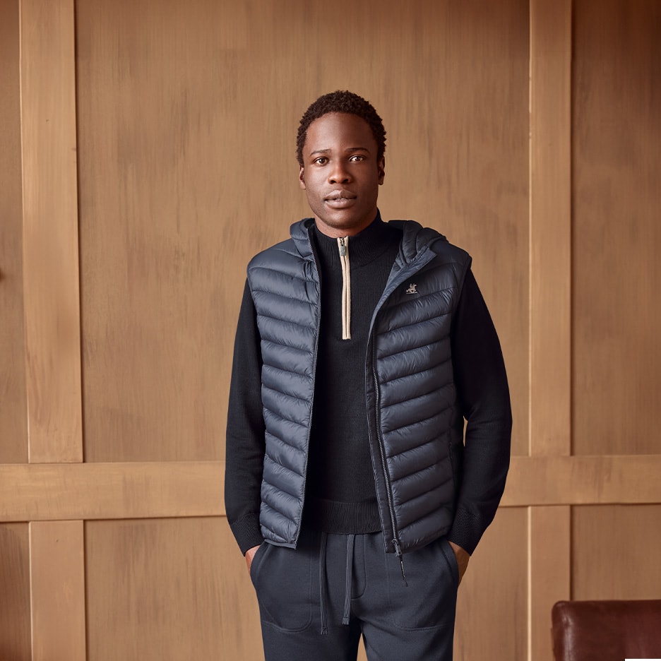 Mann in grauer Steppweste, schwarzem Rollkragenpullover und Jogginghose.